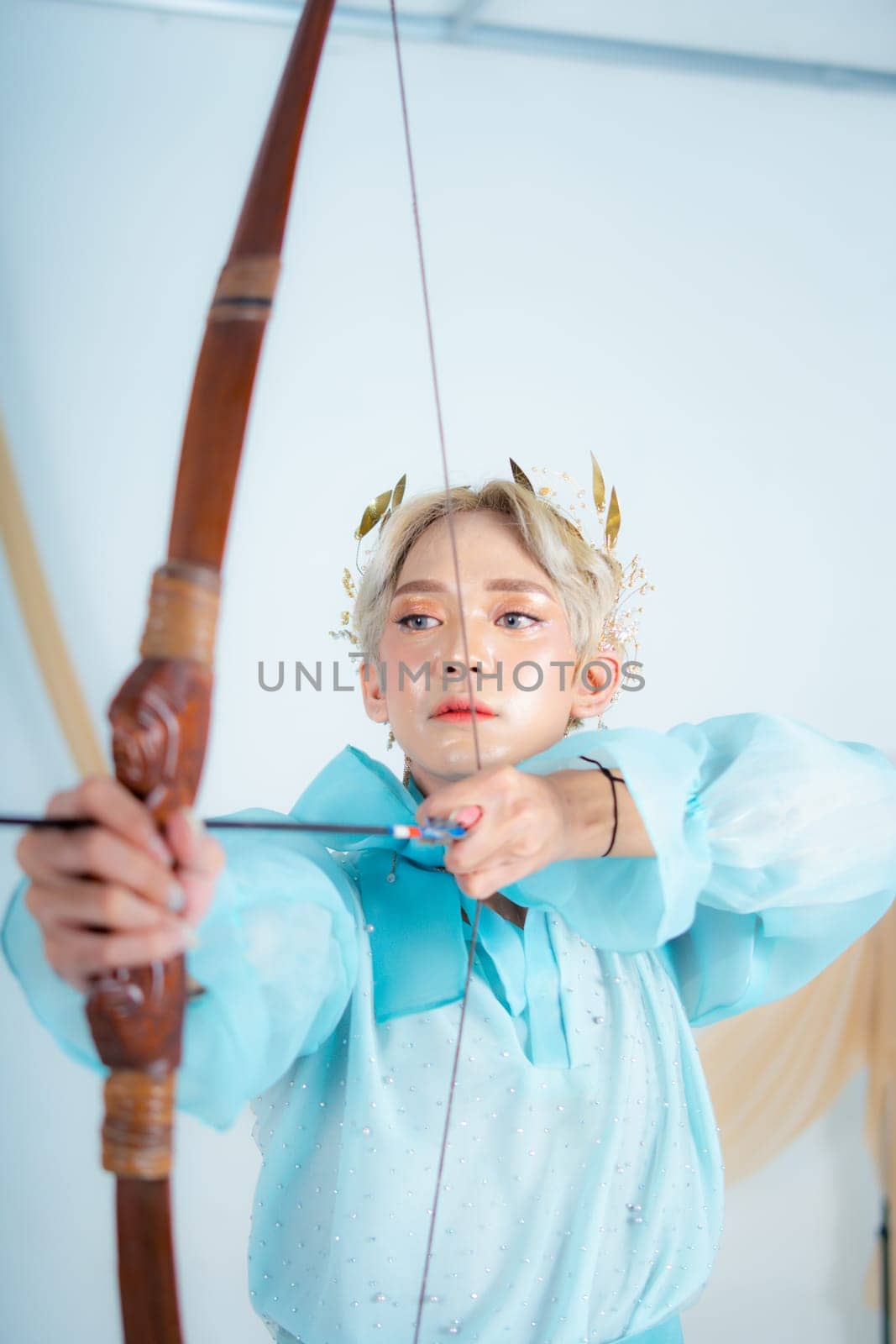 a princess in a blue dress pulling a bow with her hand in a white room