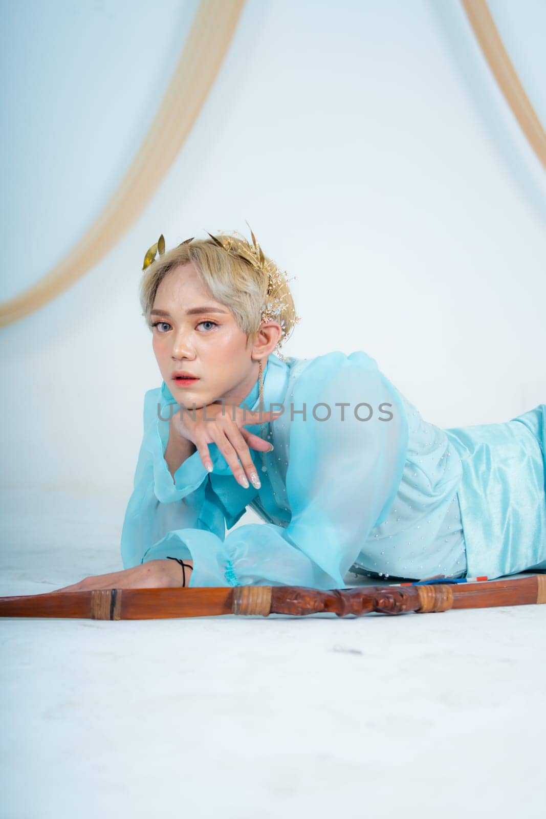 a woman with blonde hair and a face full of makeup poses beautifully with a bow in a white studio