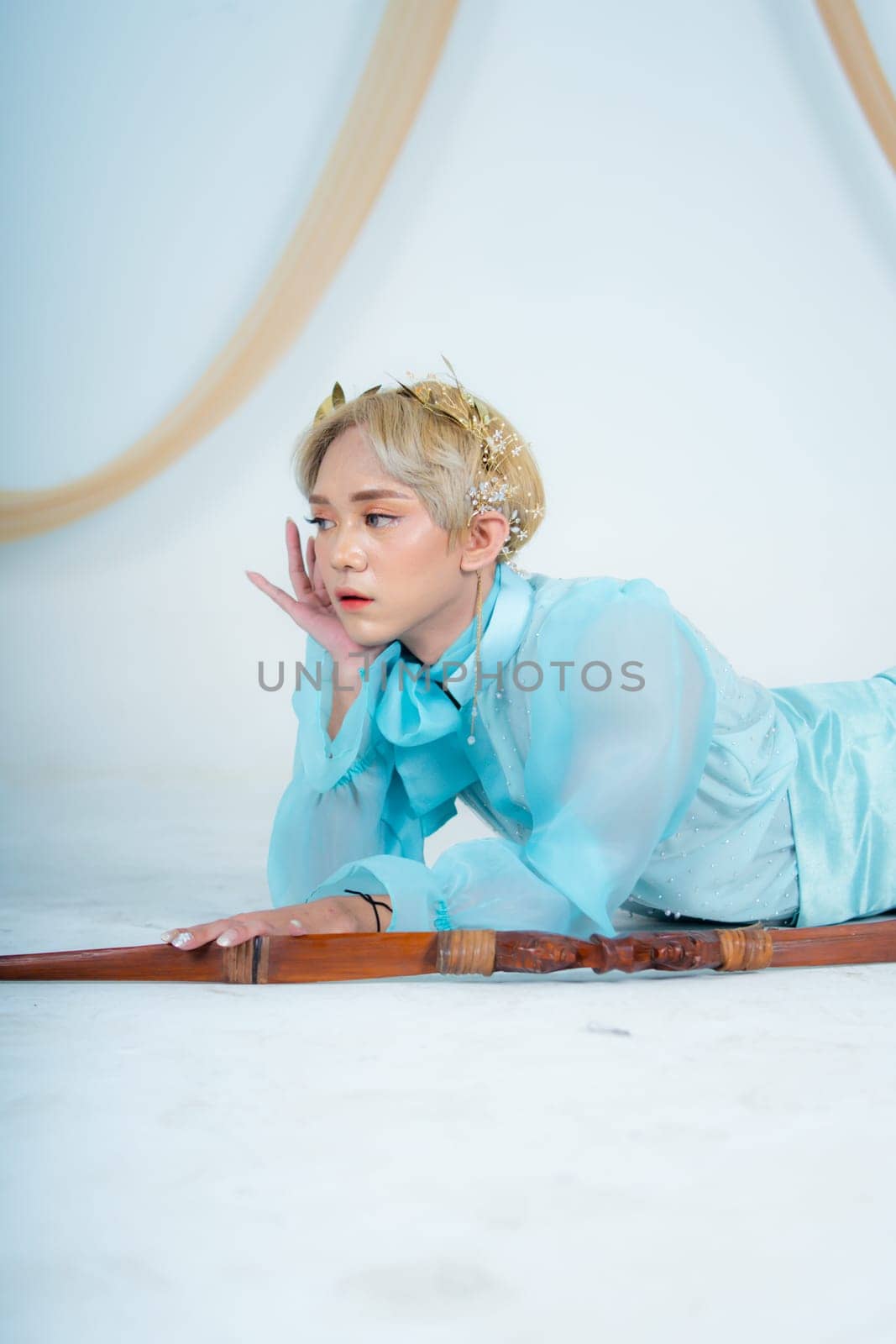a princess in a blue dress posing on the floor with a bow in a white room