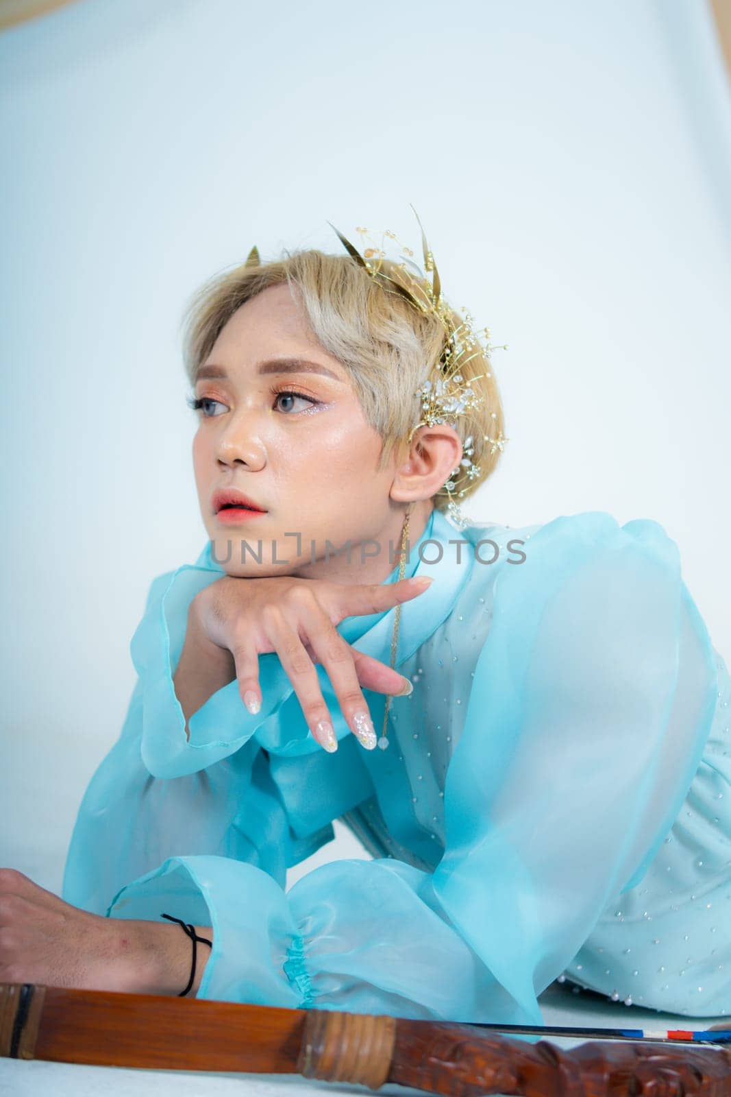 a woman with blonde hair and a face full of makeup poses beautifully with a bow in a white studio