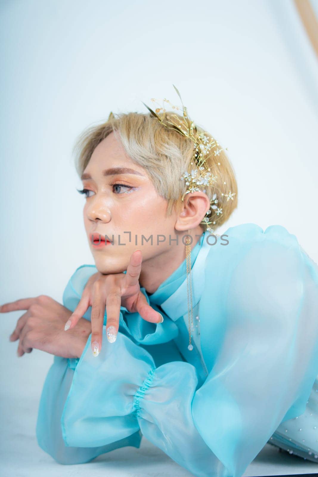 a woman with blonde hair and a blue dress posing with curled arms and a blushing face in front of a white background
