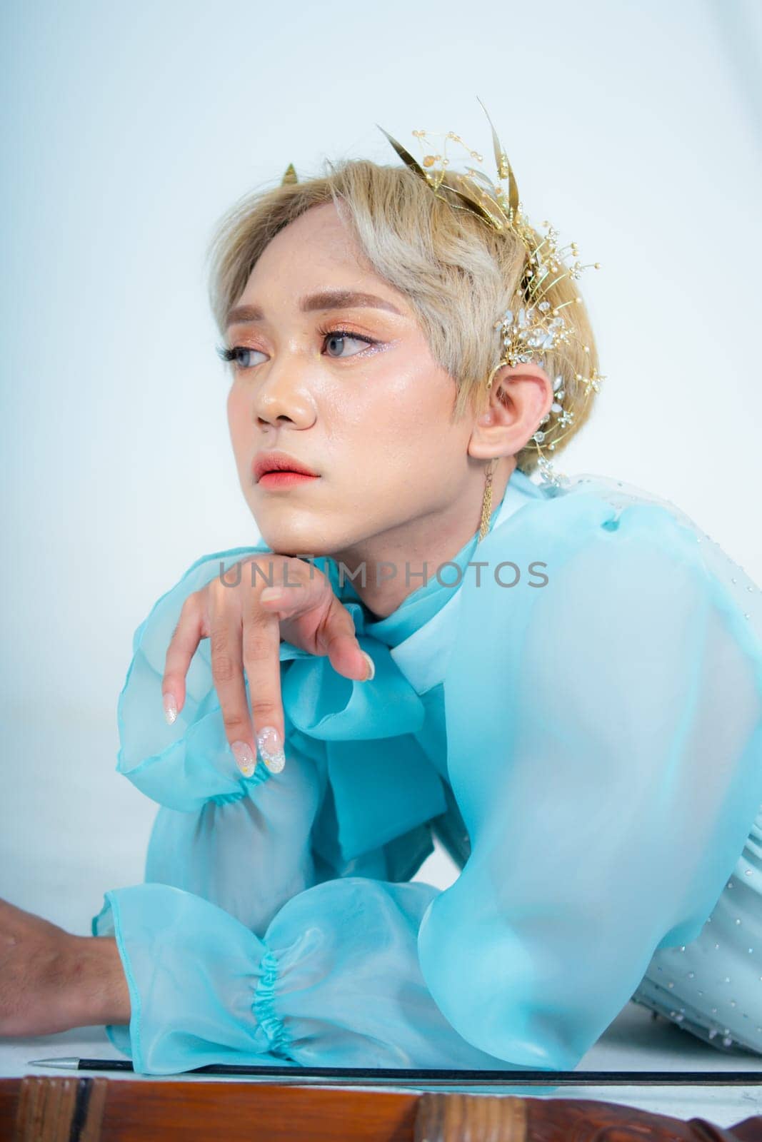 a woman with blonde hair and a blue dress posing with curled arms and a blushing face in front of a white background