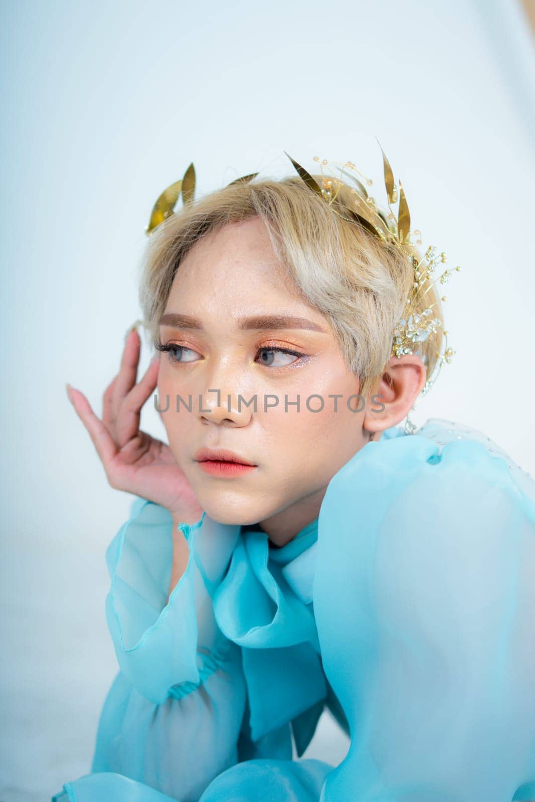 a woman with blonde hair and a blue dress posing with curled arms and a blushing face in front of a white background