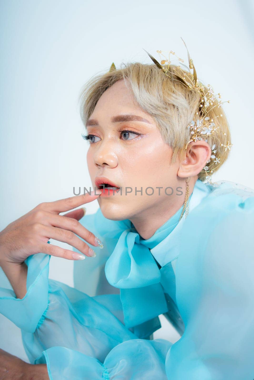 a woman with blonde hair and a blue dress posing with curled arms and a blushing face in front of a white background