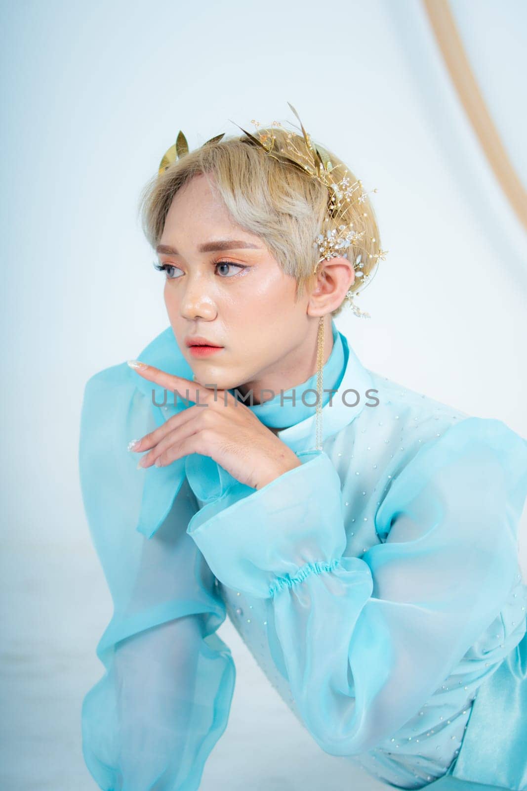 a royal princess posing with a golden crown and blonde hair very cutely in a white room