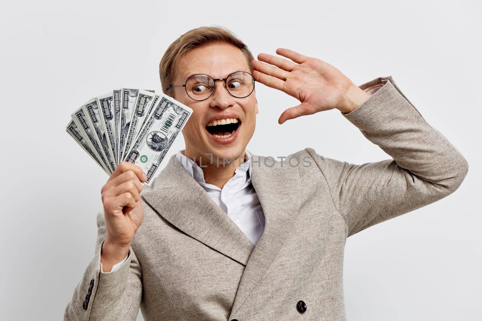 Happy man in glasses and suit celebrating financial success, smiling broadly, holding a fan of dollar bills, on plain white background. Concept: financial prosperity and victory.