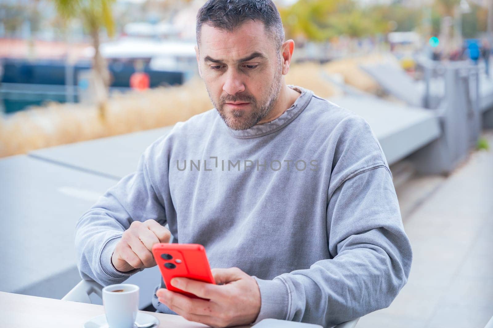 serious caucasian man, serious man looking at her mobile smart phone, typing a message on the terrace of an outdoor cafe. Addiction to social networks. App, device technology concept.