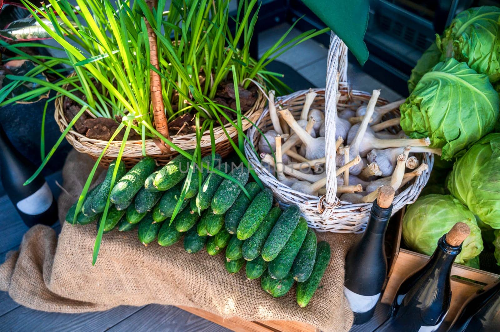 Close-up of a farmer's market stall with fresh green vegetables. Cucumbers, young cabbage, garlic in a basket, bottles of wine, young onions. Healthy vegetarian ingredients. Various clean vegetables