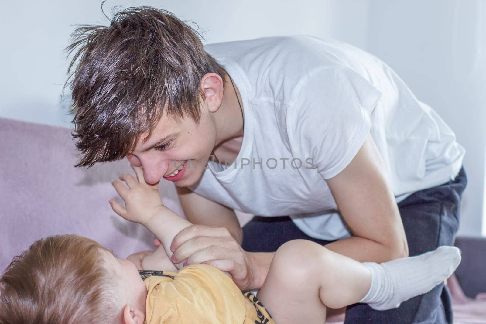 Teenage boy happily playing with his younger brother while looking after him. High quality photo