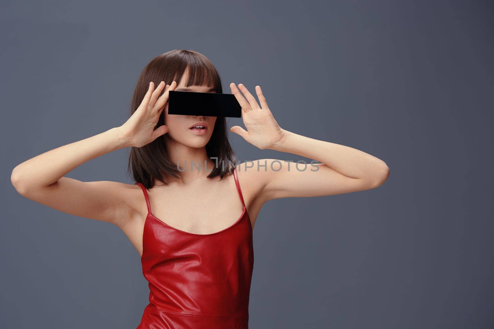 Woman in a red dress covering eyes with black phone against gray background