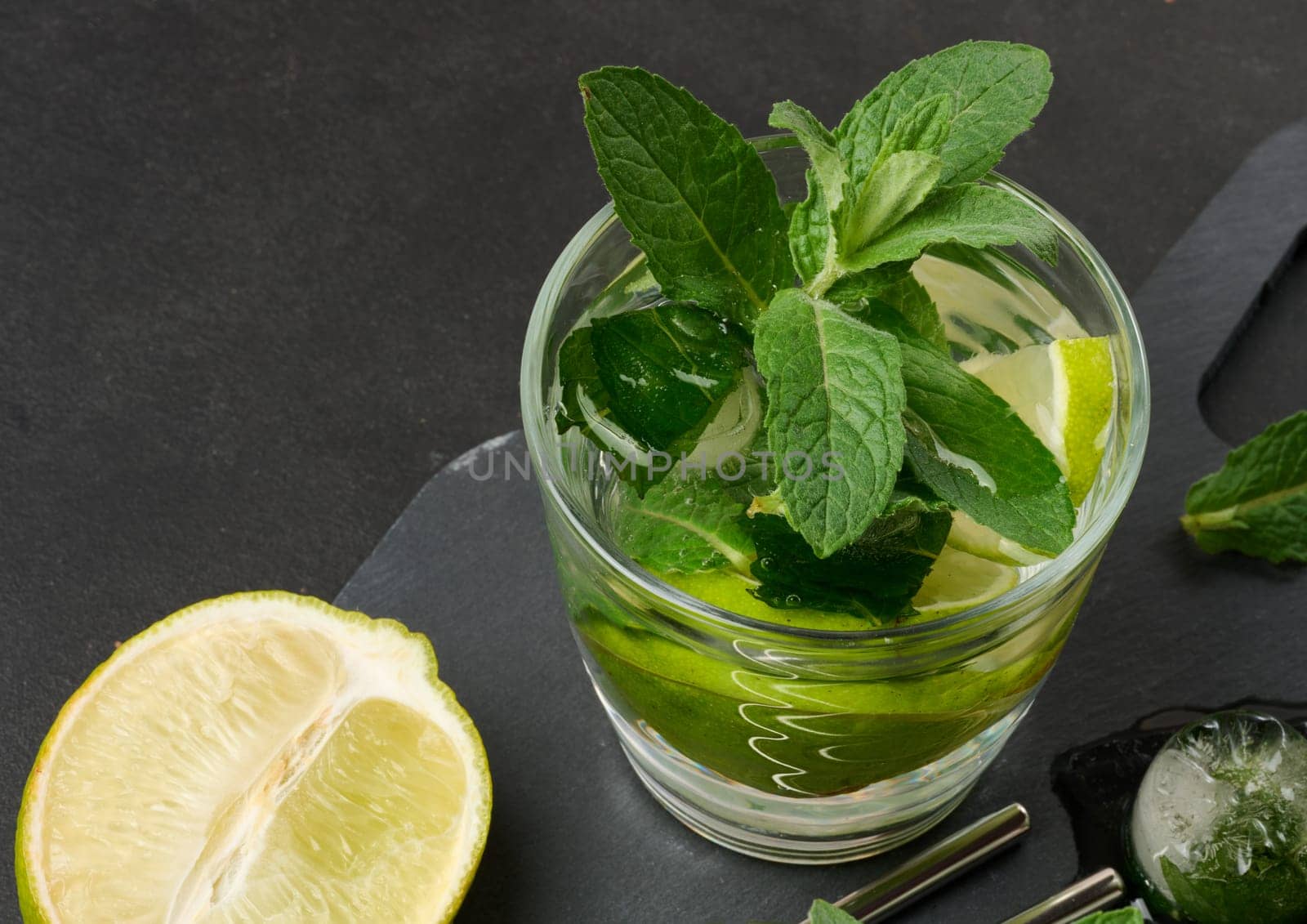 Refreshing mojito cocktail with lime, mint, strawberry, and ice on dark background, top view