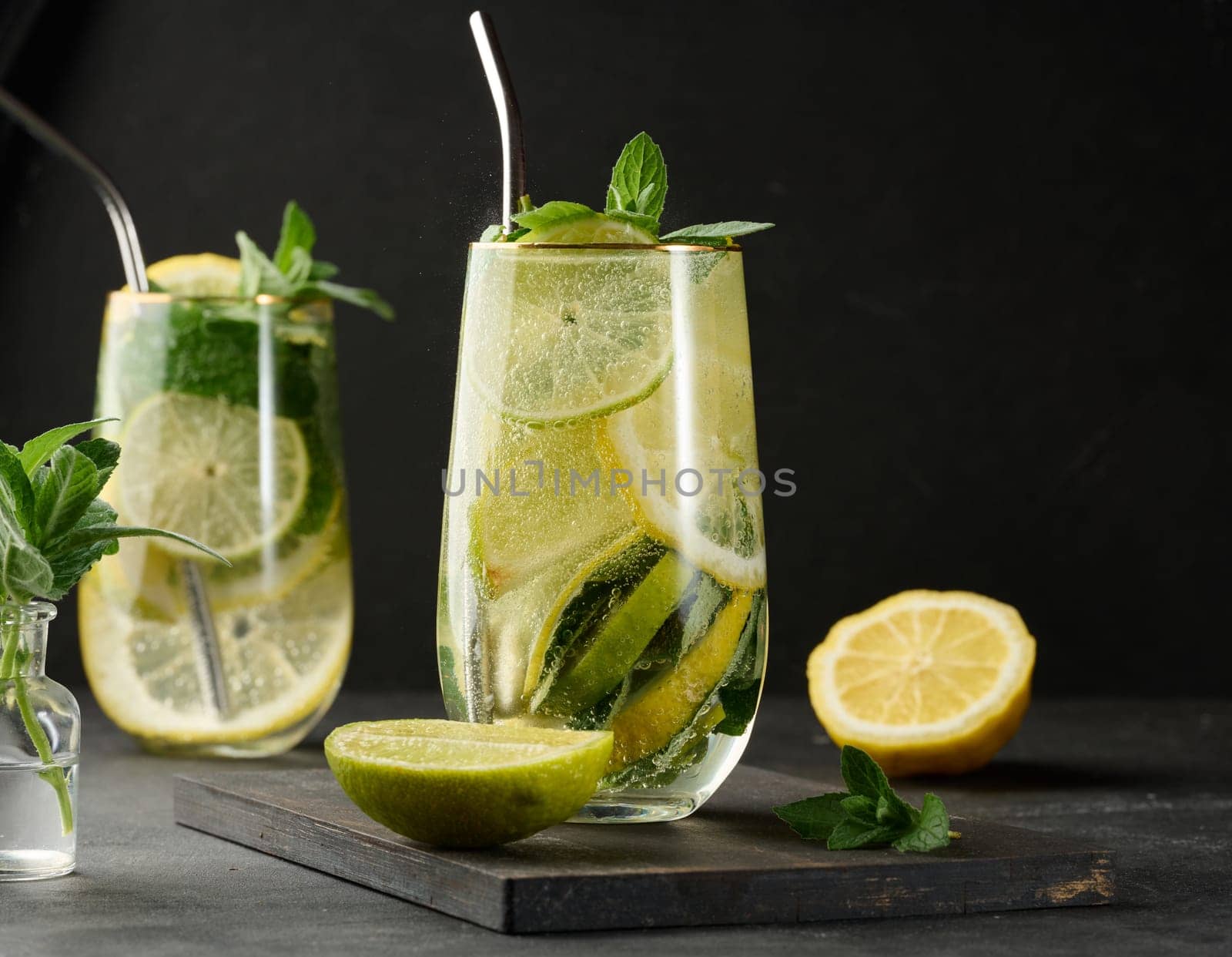 Refreshing detox or summer drink in a glass with lemon, lime, mint, ice, and metal straw. Dark background