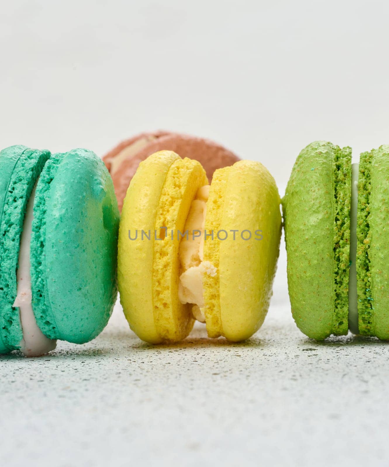 An assortment of colorful macarons on a white surface with dark speckles. The macarons have a smooth, delicate shell and a creamy filling