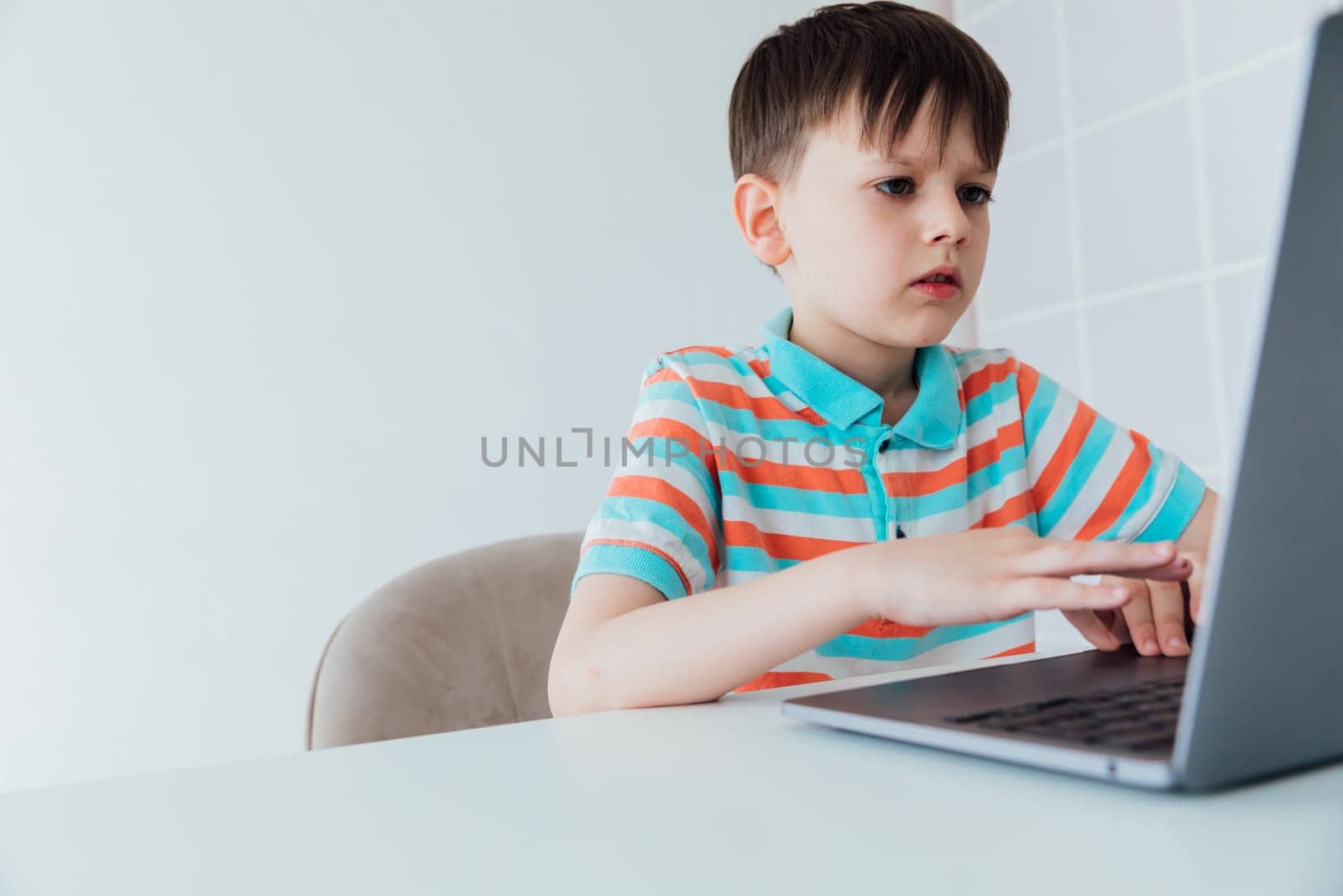 Boy schoolboy learning games at the table with laptop online