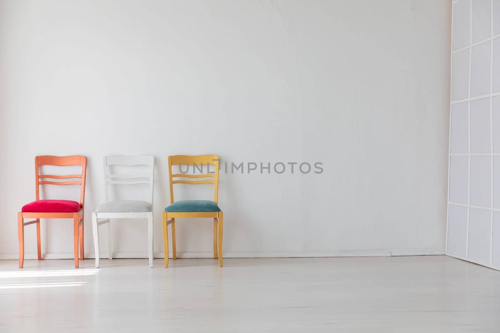 Three chairs of different colors in the interior of a white room