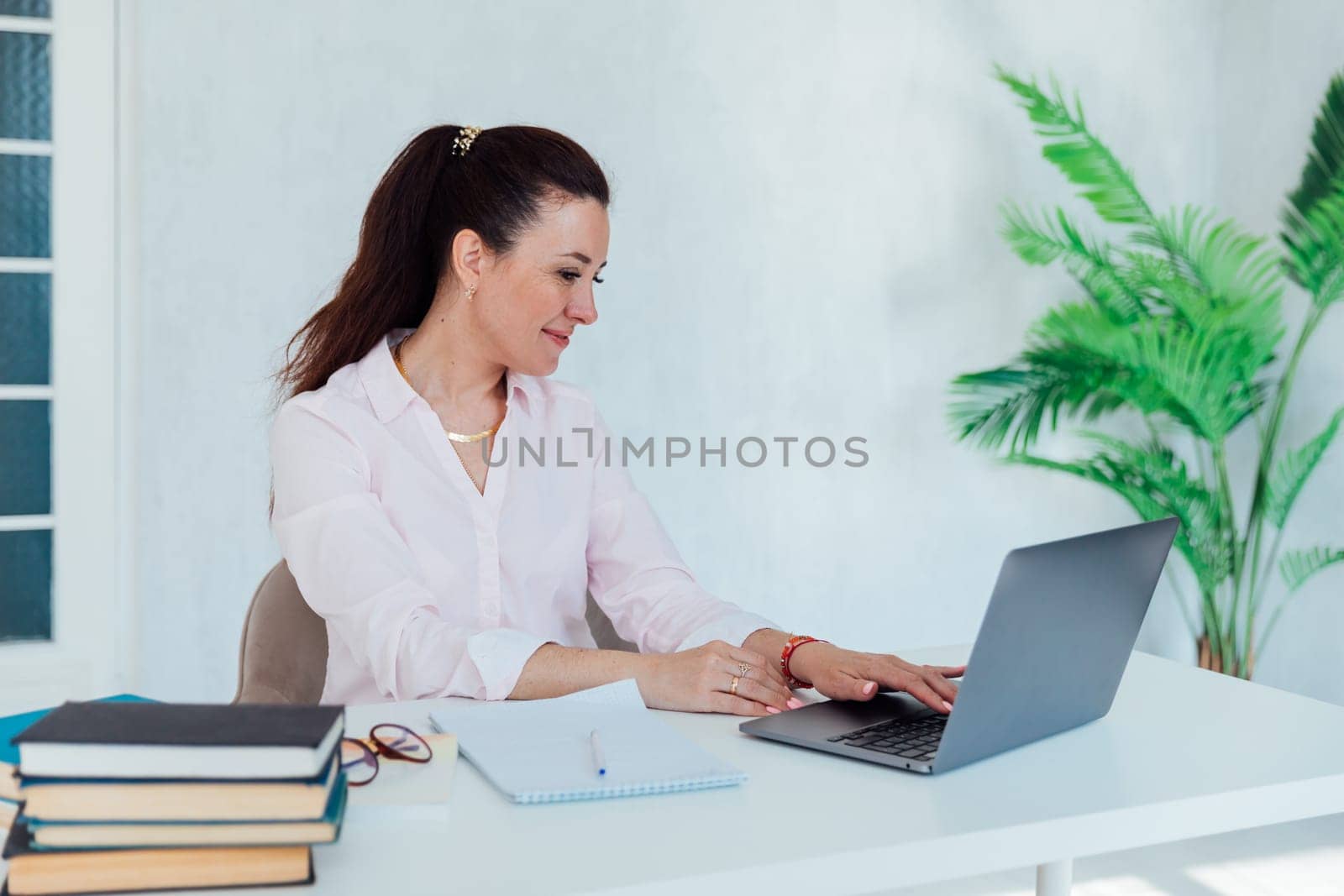 brunette woman working in office at desk with laptop and documents