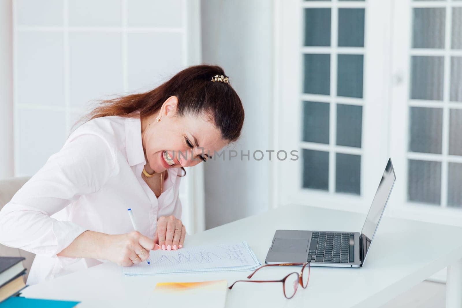 brunette woman nervous writing at office desk with laptop