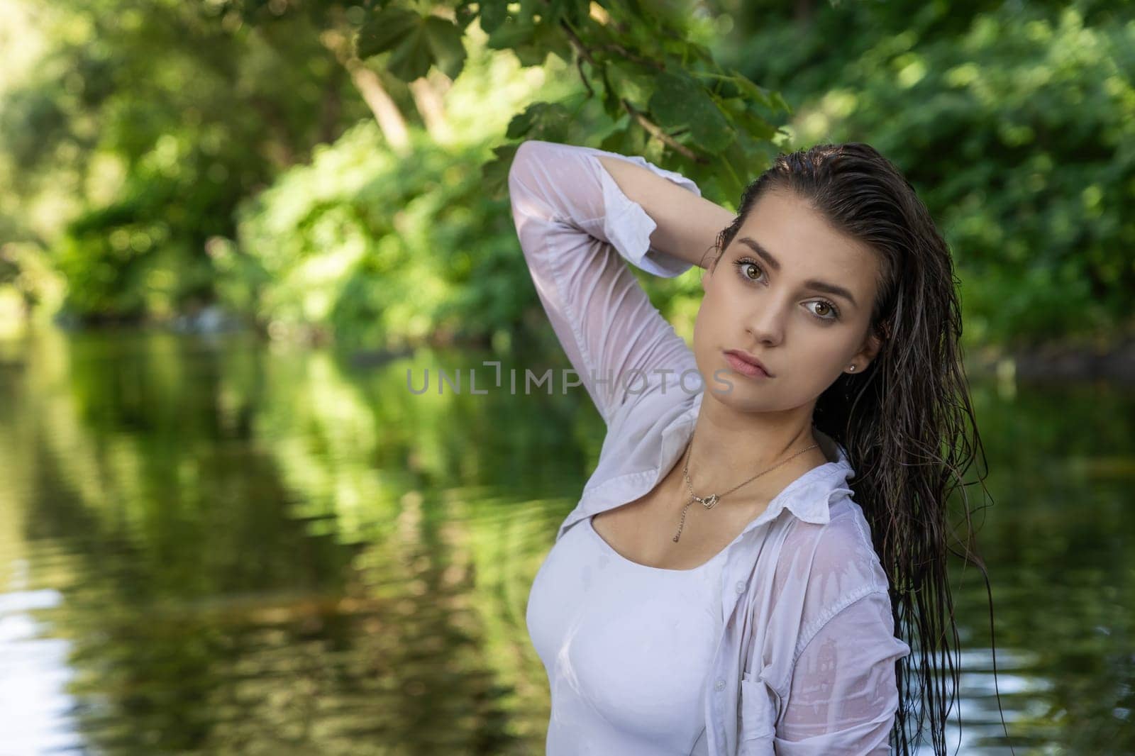 Moody portrait of beautiful brunette girl with wet hair posing in the river. Horizontally. 
