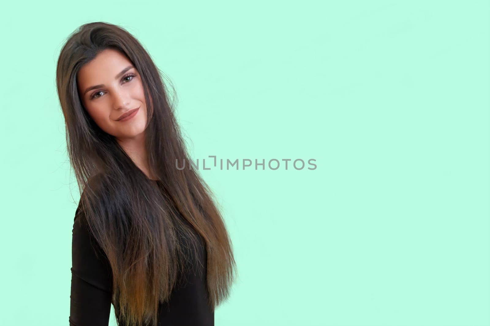 Studio waist up portrait of a tanned beautiful brunette long haired young  woman posing in front of a light green background.