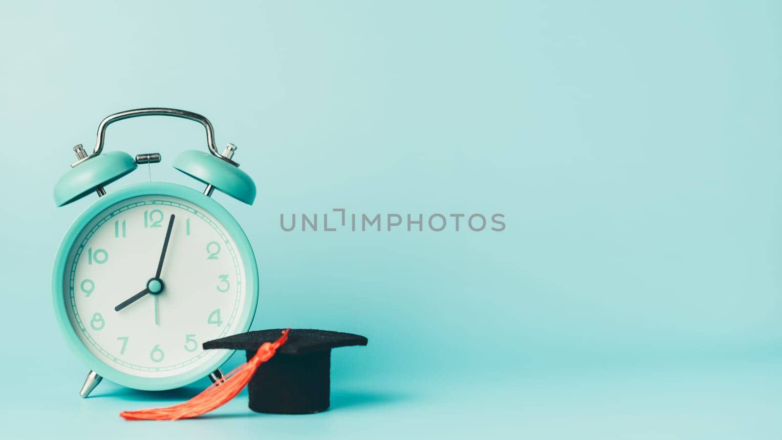 Graduation cap and alarm clock on blue background. Symbol of education, time management, exam preparation, academic success, and back to school concept.