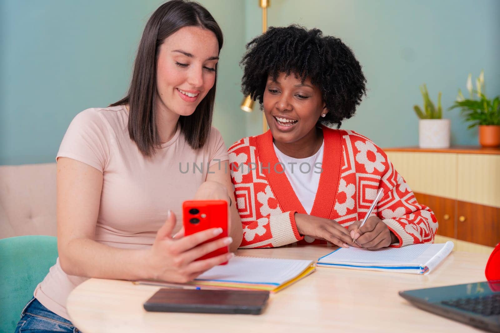 Caucasian and African American friends share a joyful moment as they look at a mobile phone together. Their smiles and relaxed vibe highlight connection, friendship, and digital engagement indoors.