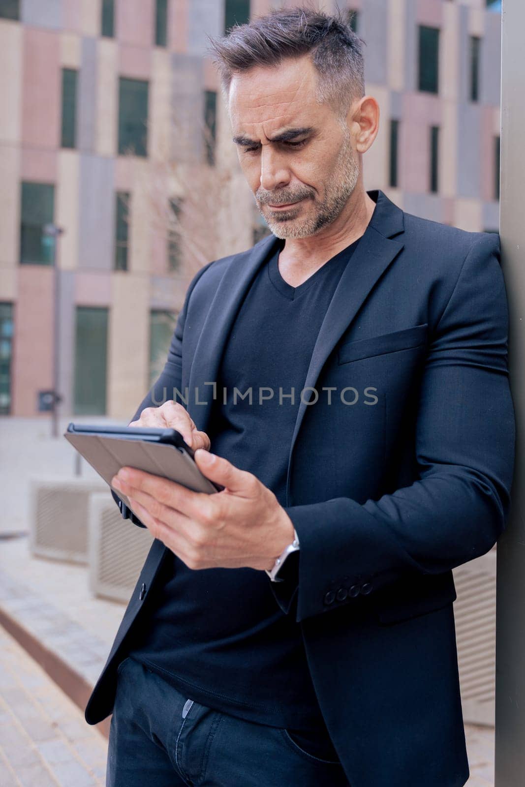 Confident businessman standing outdoors using a tablet in a modern urban setting.He appears focused and professional. Concept of digital work, technology, and contemporary business lifestyle. Vertical