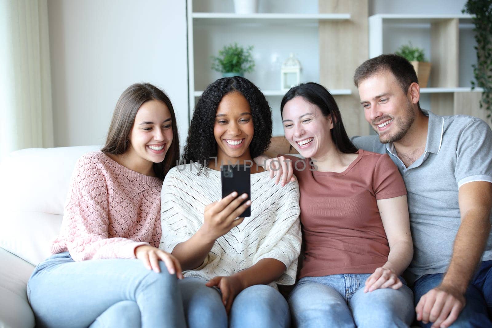 Four interracial friends at home checking mobile phone on a couch