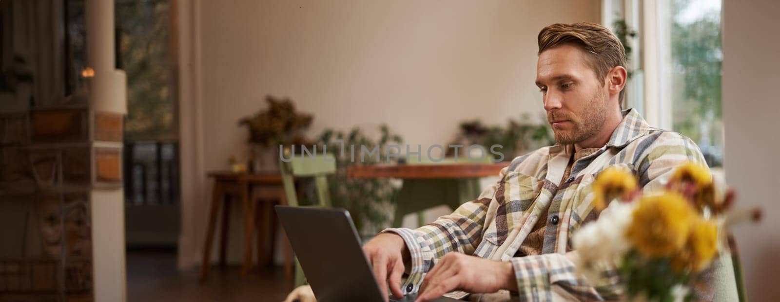 Lifestyle and workplace concept. Young handsome man in casual clothes, sitting in cafe with laptop, studying online, working remotely from coffee shop.
