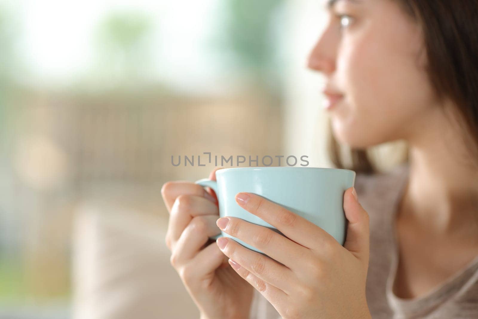 Close up portrait of a woman holding coffee mug looking at side at home
