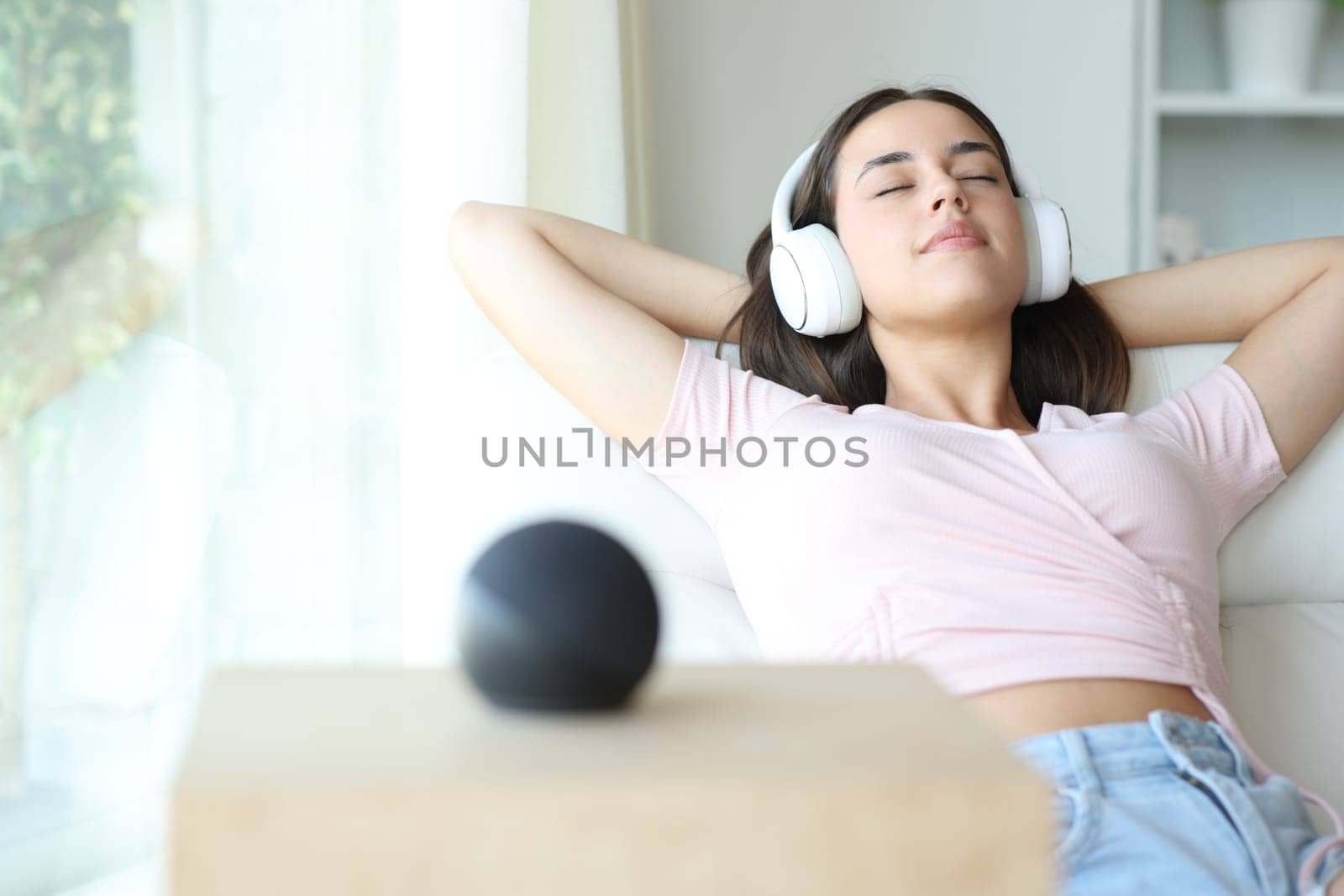Woman relaxing listening music with headphone and smart speaker sitting on a sofa at home