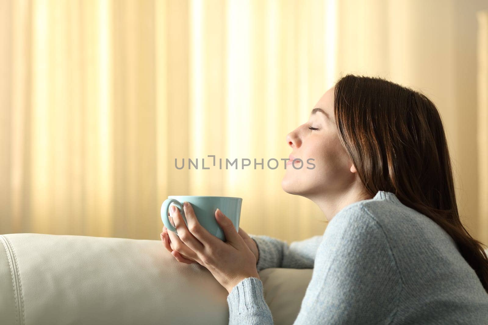 Profile of a woman at home smelling coffee aroma in the living room