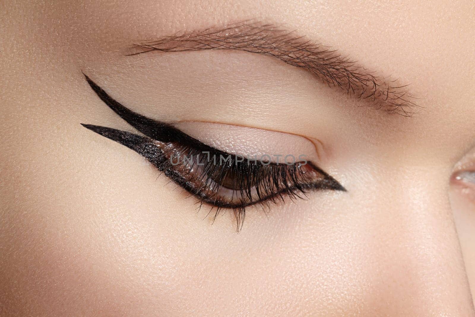 Beautiful macro shot of female eye with classic eyeliner makeup. Perfect shape of eyebrows, brown eyeshadows and long eyelashes. Cosmetics and make-up. Closeup macro shot of fashion liner eyes visage