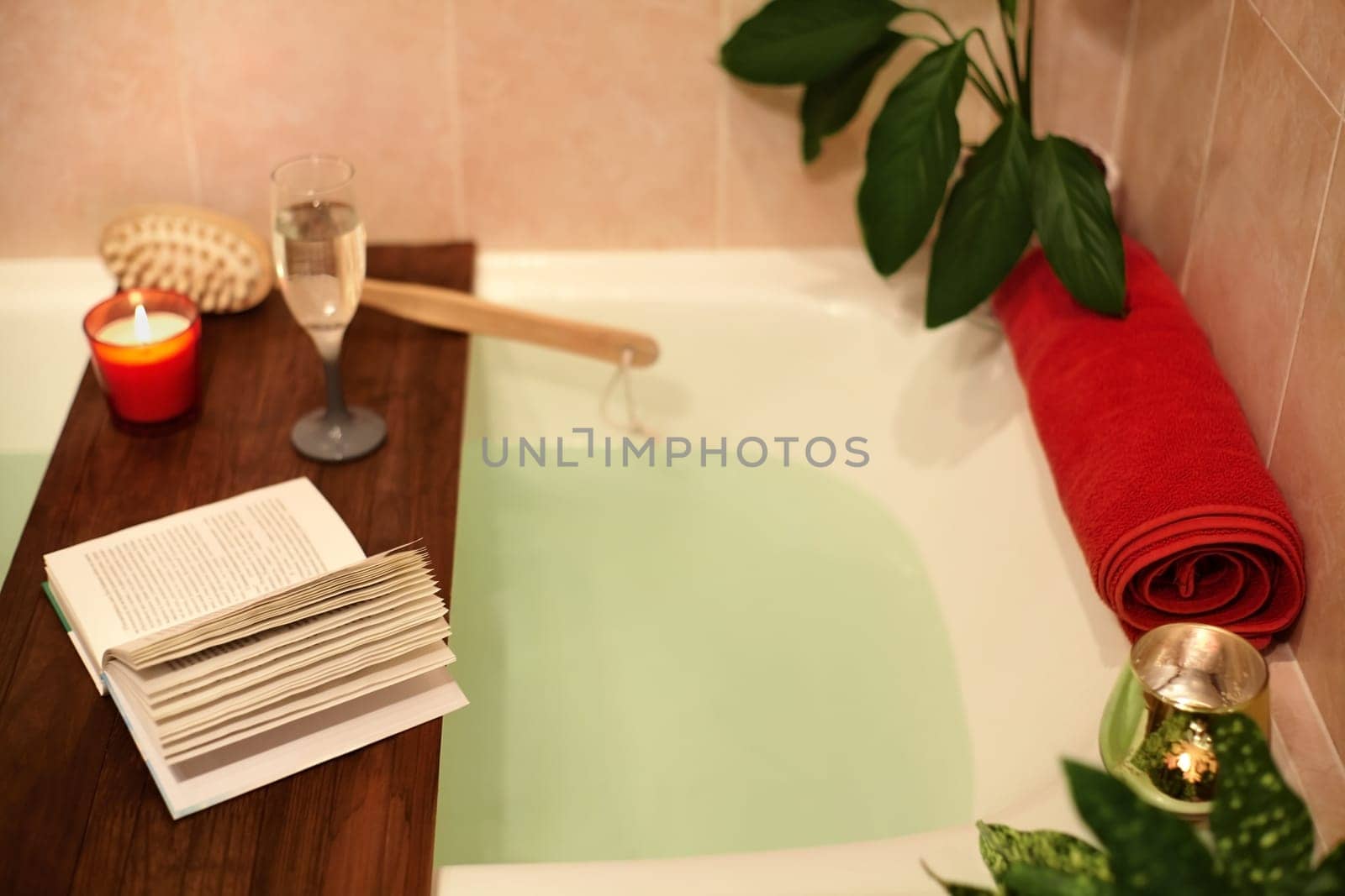Time for Yourself. Relax at home. Bath tub with flower petals. Book, candles and glass of wine on a wood tray. Organic Spa Relaxation in comfort cozy bathroom