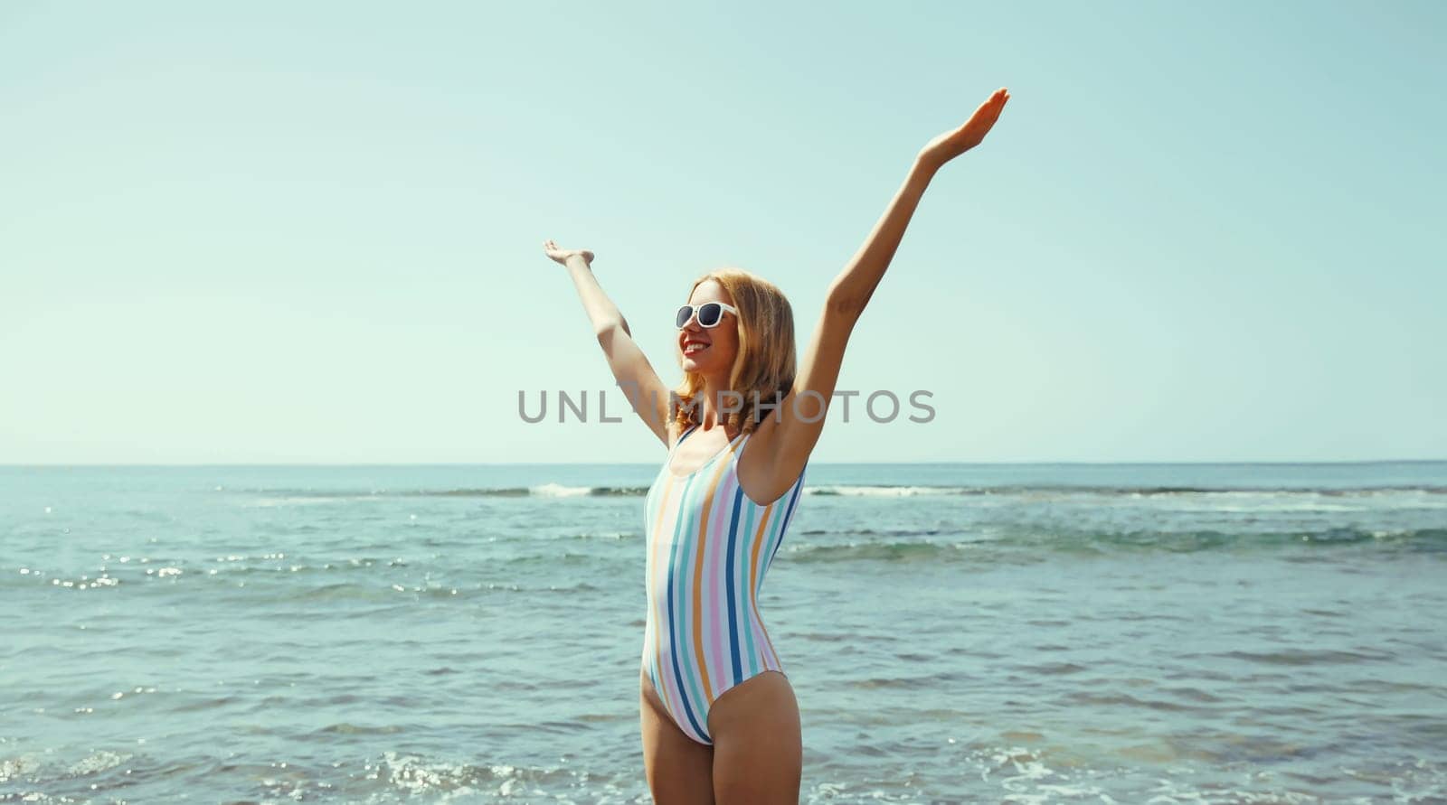 Summer vacation, beautiful happy slim cheerful woman in swimsuit having fun on the beach on sunny day on sea coast with waves background