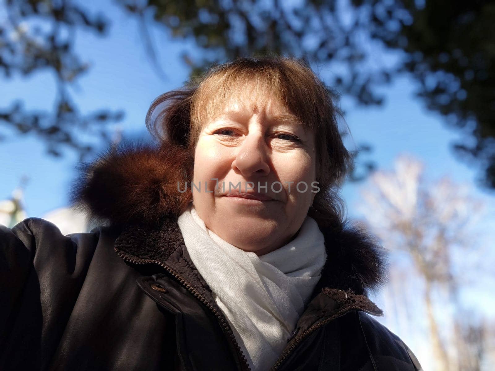A middle aged woman with blonde hair takes a selfie outdoors, enjoying the beautiful weather while exploring the surroundings.
