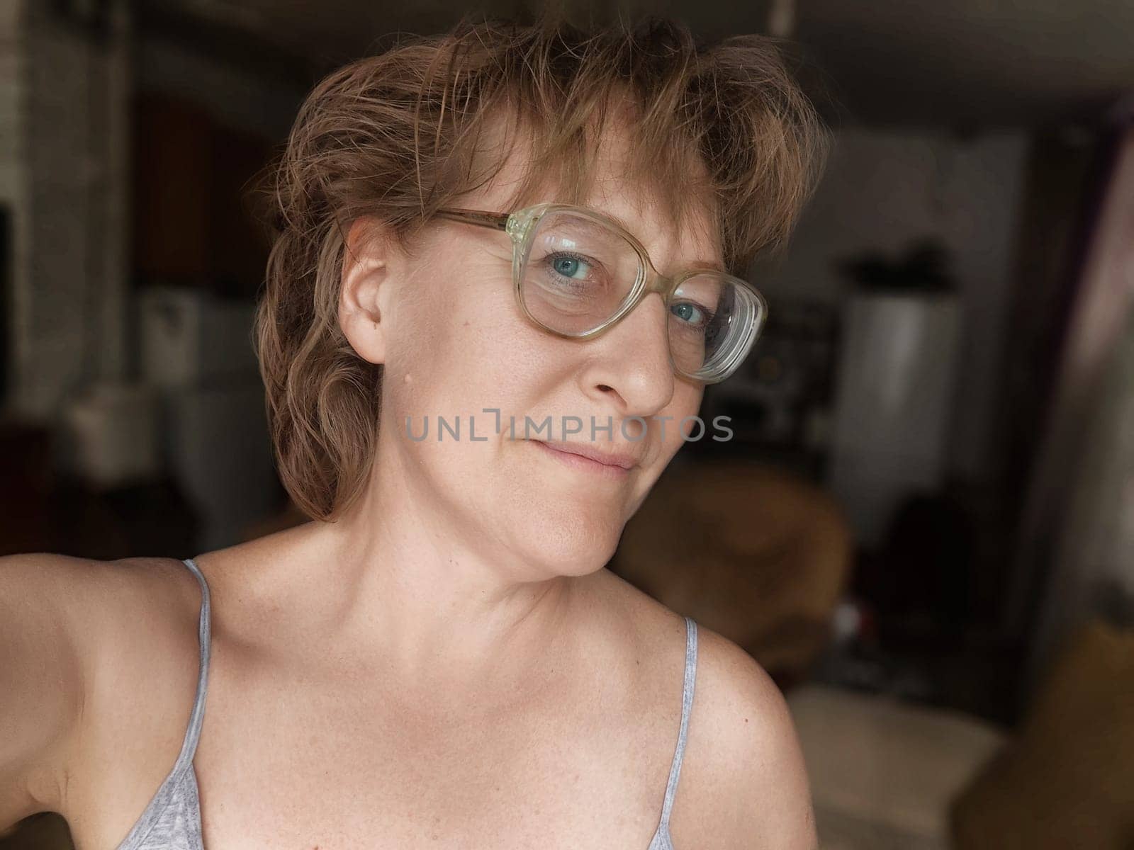 Mature woman with glasses enjoys a selfie moment in a relaxed indoor environment, sharing her lifestyle with her followers.