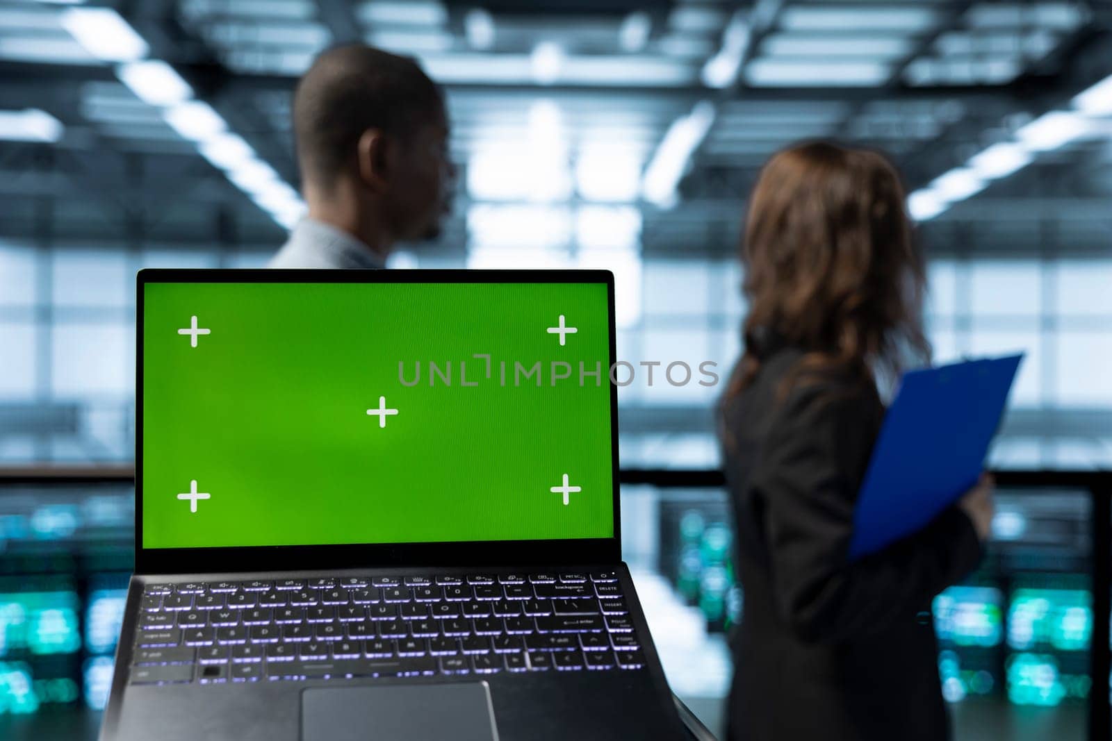 Focus on isolated screen laptop in front of engineers in blurry background doing network virtualization. Close up of mockup chroma key notebook used by admins in server farm verifying settings