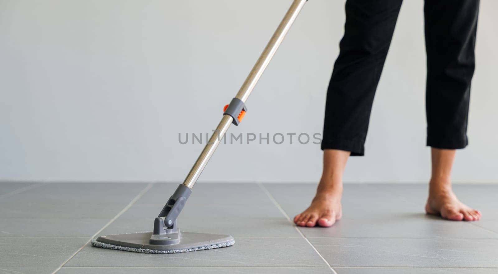 Woman mops the indoor floor, cleaning the front area of her home with a mop and rag. Housewife dedicated to maintaining cleanliness. Represents professional housekeeping and house maintenance concepts