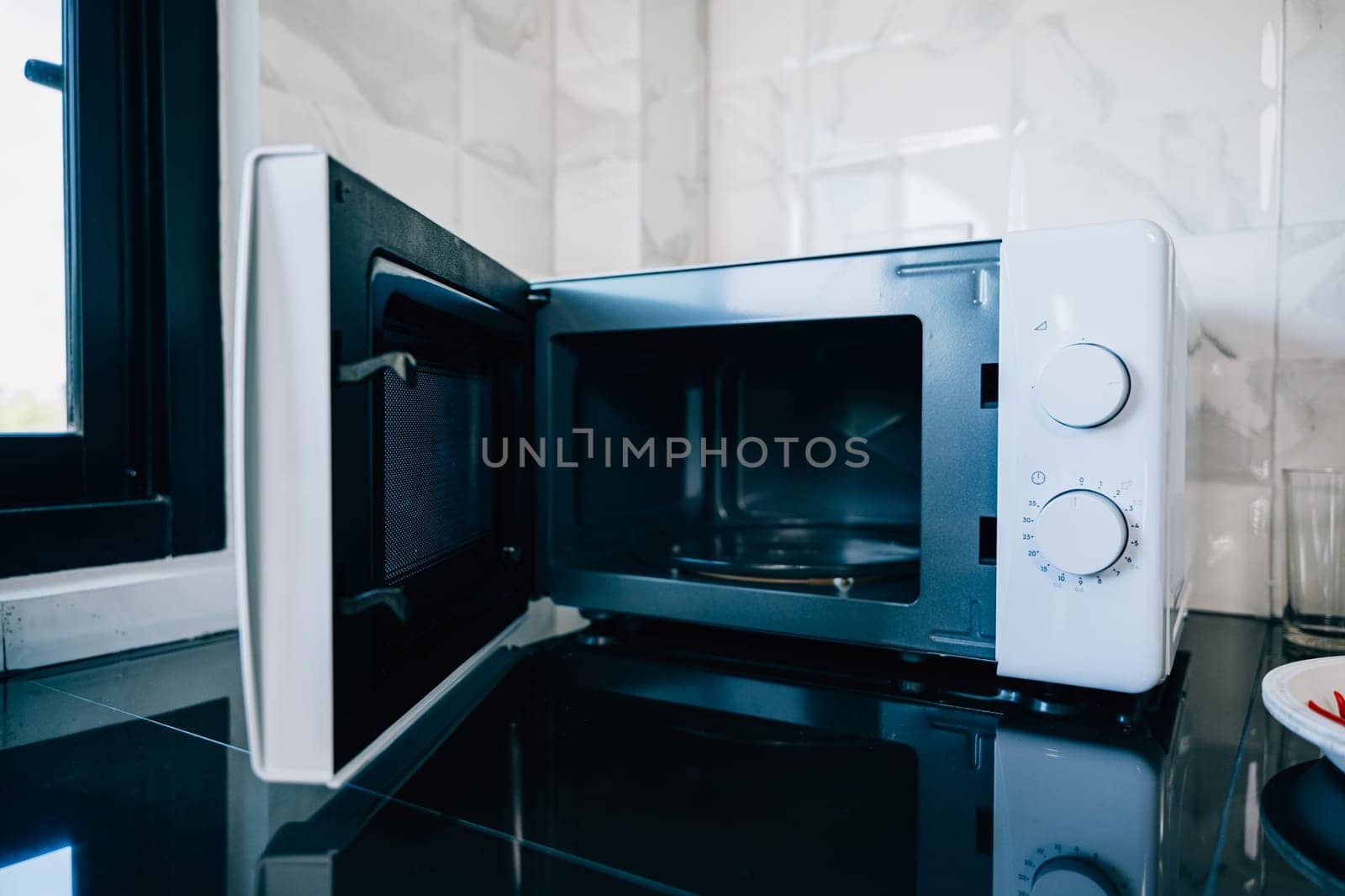 An open microwave oven door on a sleek kitchen tabletop presenting modern technology and design in household appliances. Perfect for showcasing contemporary kitchen equipment.