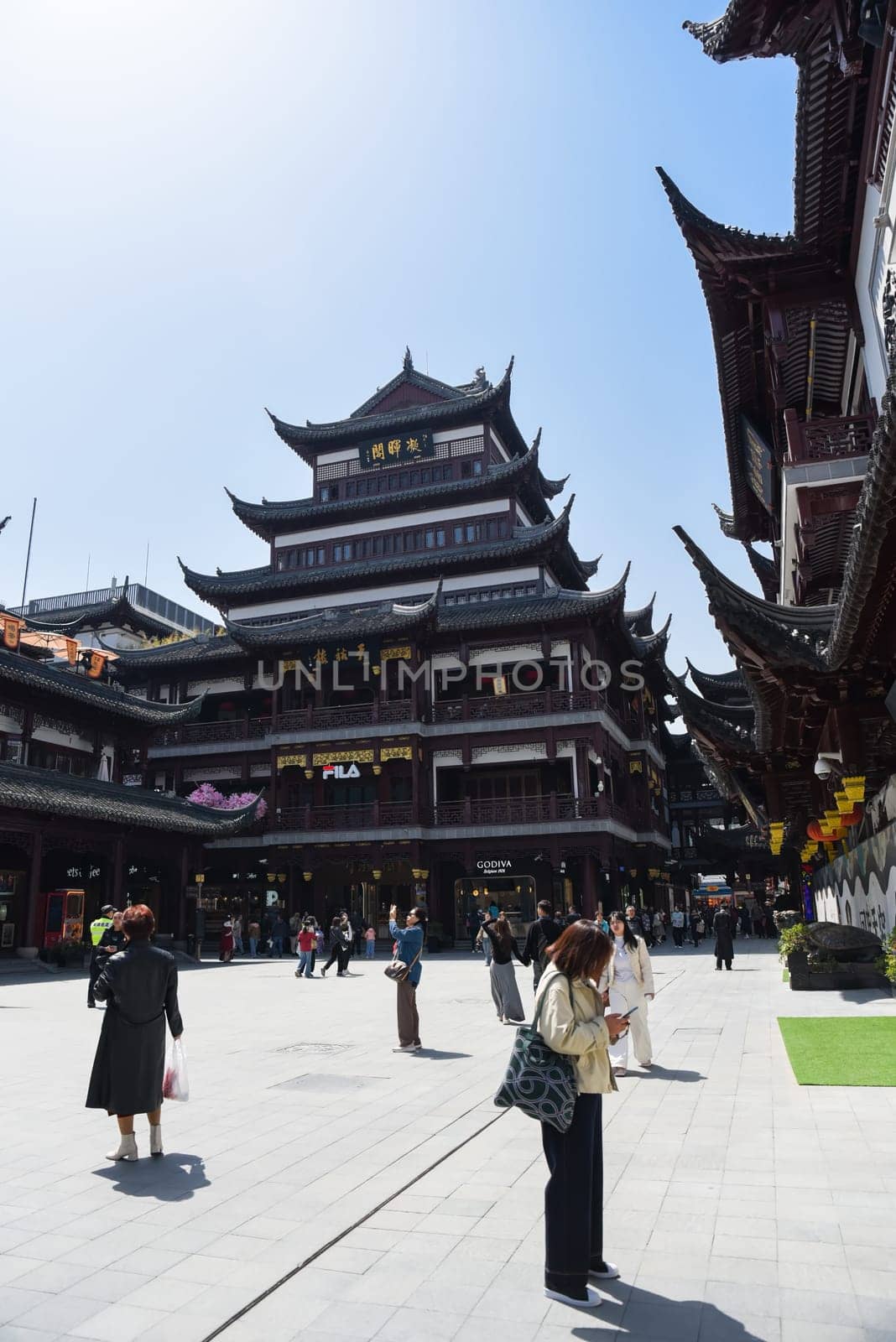 Shanghai, China - 1 April 2025: Tourists walk around the central plaza of Yuyuan Old Street, surrounded by traditional Chinese architecture under clear blue skies