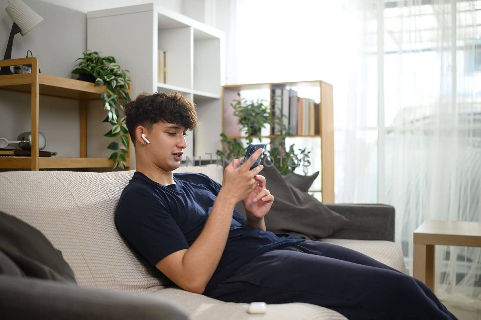 Man in loungewear enjoying a call or music with wireless earbuds on a couch.