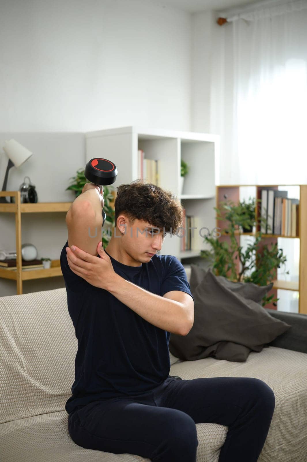 Young man lifting dumbbells on a sofa. Fitness at home concept.