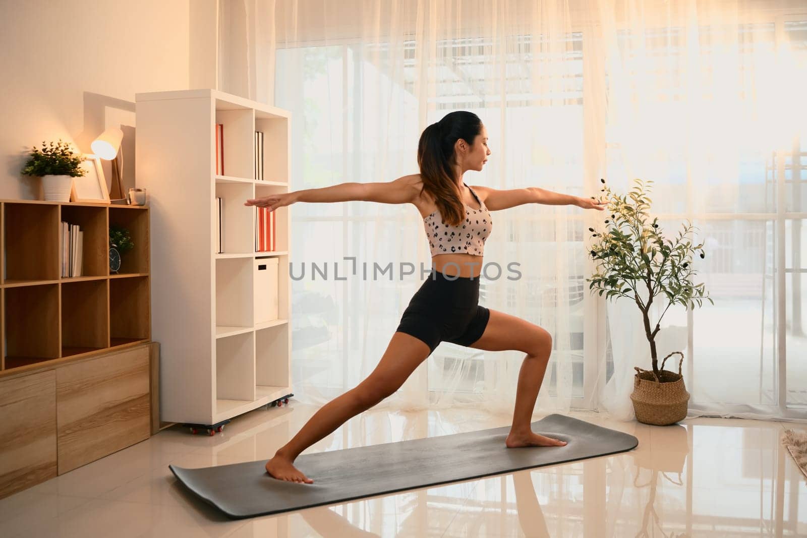Young woman performing warrior pose on a yoga mat in a living room.