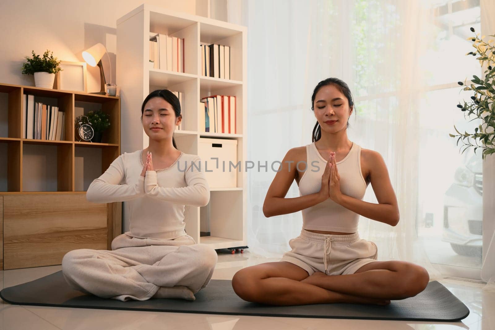 Calm and focused mother and daughter practicing yoga together in a peaceful indoor.
