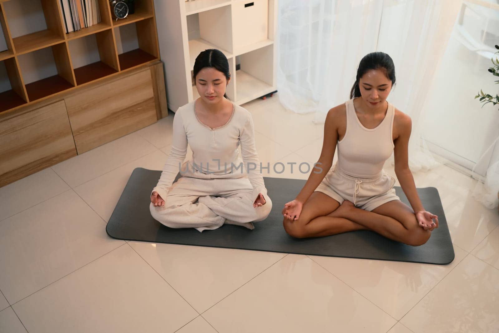 Calm and focused mother and daughter practicing yoga together in a peaceful indoor.
