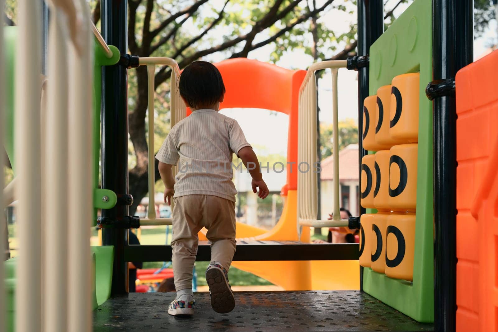 Back view of toddler enjoying playtime at a colorful outdoor playground.