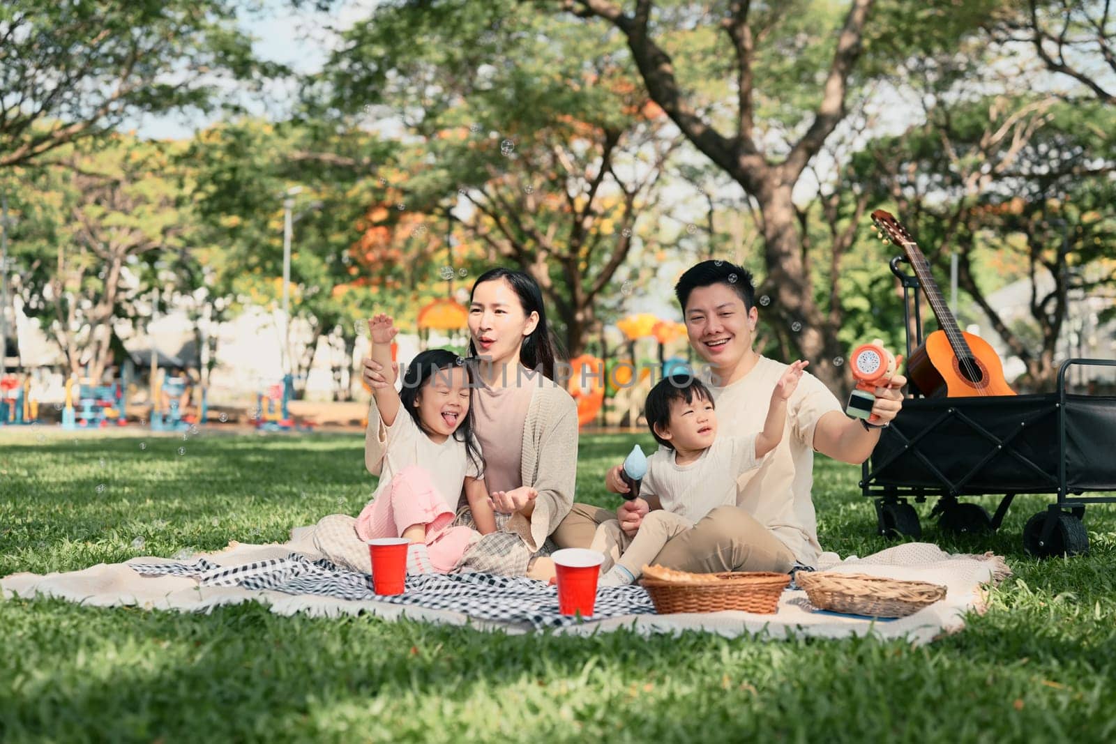 Happy family having a picnic and playing with bubbles together at the park.