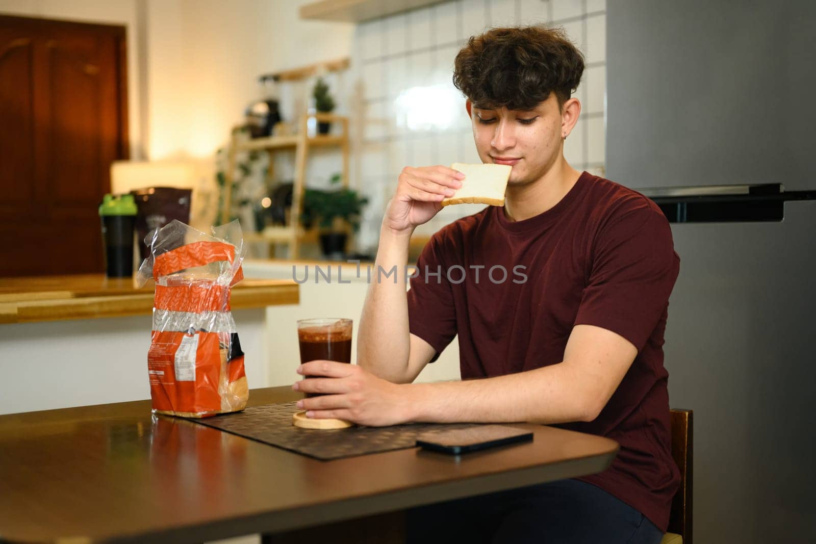 Casual morning routine of man having bread and drink in a cozy kitchen.
