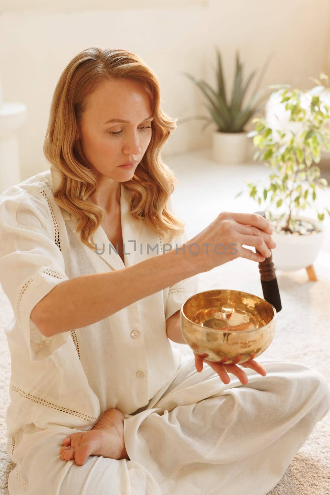 Woman using a Tibetan singing bowl during sound therapy session, practicing mindfulness in a calming space.