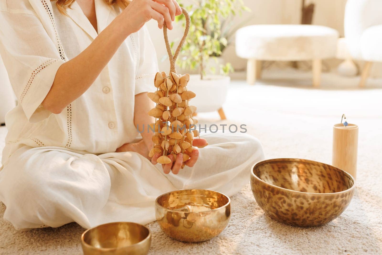 Woman practicing sound healing with seed shaker, surrounded by singing bowls in calm, peaceful home setting.
